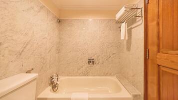 A bathroom with a marble wall, a bathtub, a wooden door, and a towel rack.