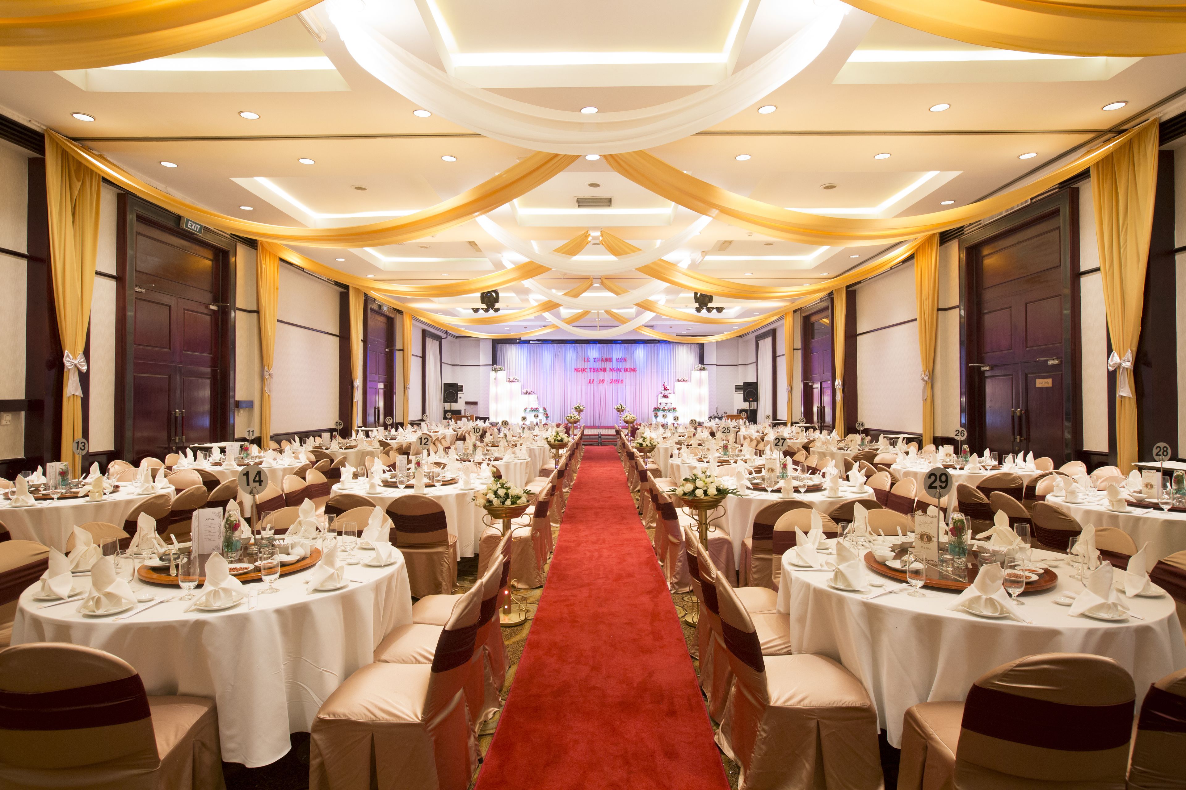 A banquet hall with round tables, white tablecloths, and red carpet.