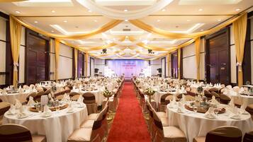 A banquet hall with round tables, white tablecloths, and red carpet.