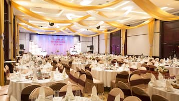 Uma sala de banquetes com mesas redondas preparadas para um evento formal, com toalhas brancas e cortinas douradas.