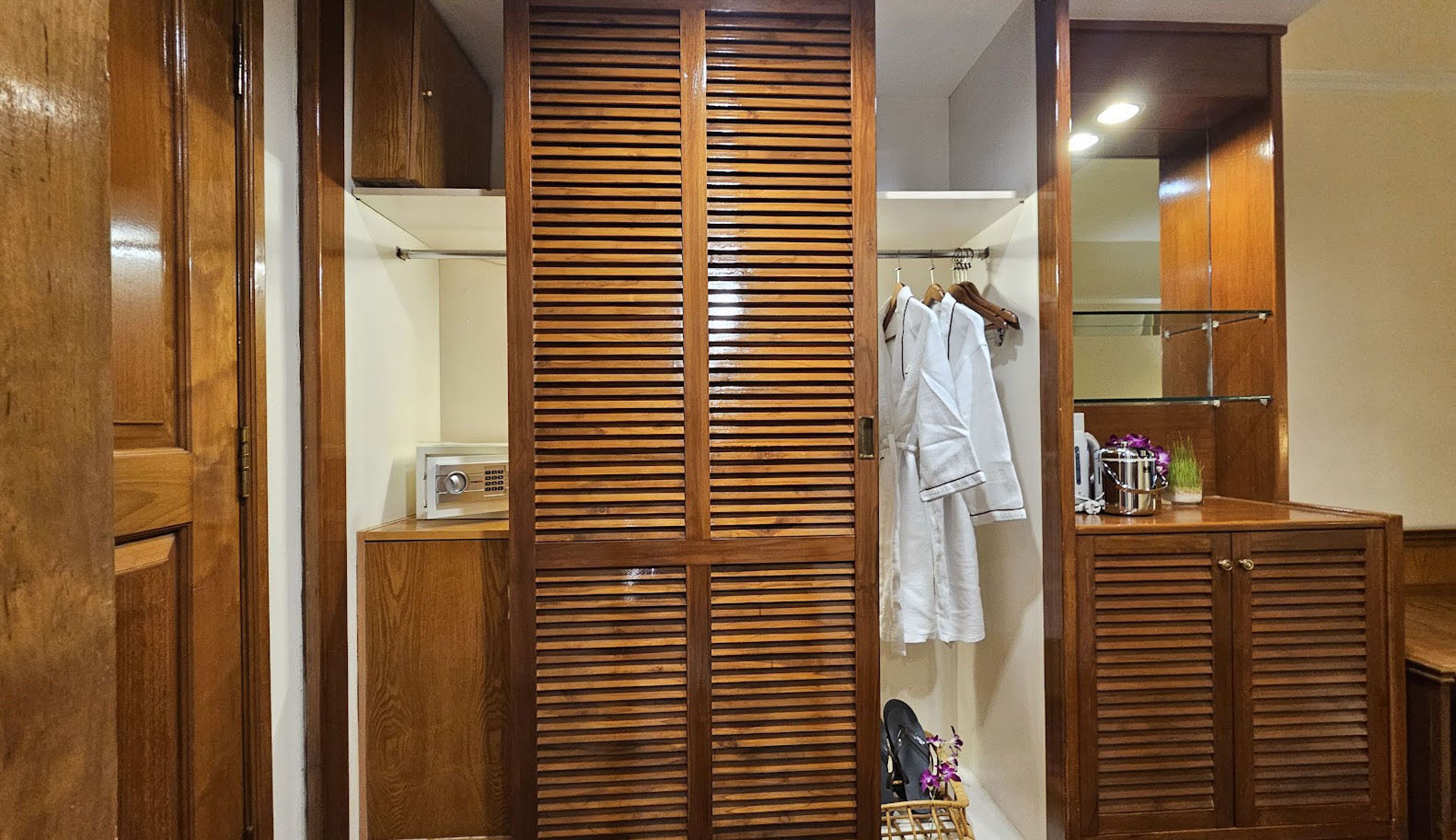 A wooden wardrobe with a mirrored closet door, a hanging robe, and a small shelf with toiletries.