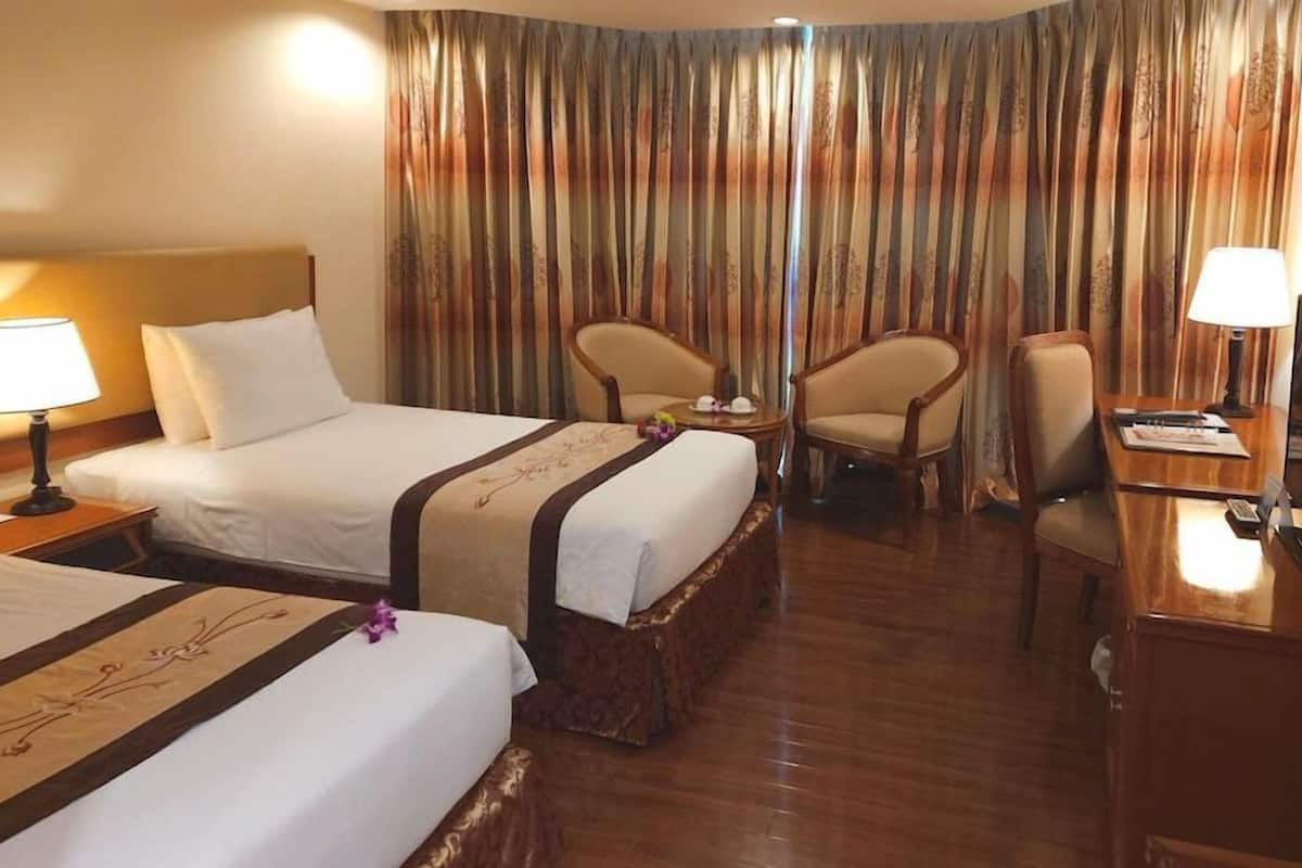 Une chambre d’hôtel avec deux lits, un bureau, une chaise, une télévision et un rideau à motifs.