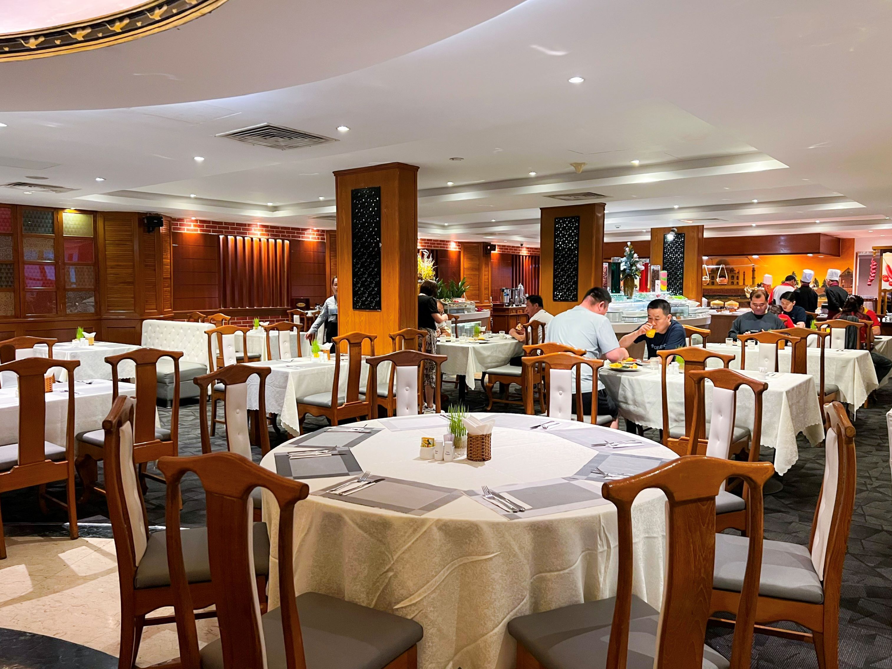 A restaurant with round tables, wooden chairs, and a high ceiling with recessed lighting.