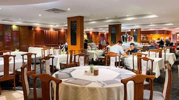 A restaurant with round tables, wooden chairs, and a high ceiling with recessed lighting.