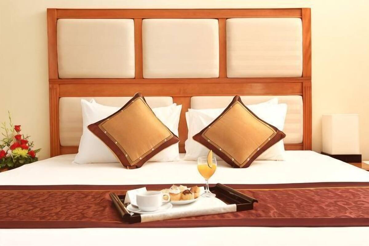 Une chambre d’hôtel avec une tête de lit en bois, deux oreillers, un plateau avec des articles pour le petit-déjeuner et une table de chevet.