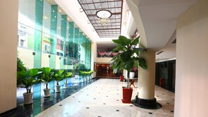 Een ruime lobby met een hoge plafond, grote ramen en potplanten.