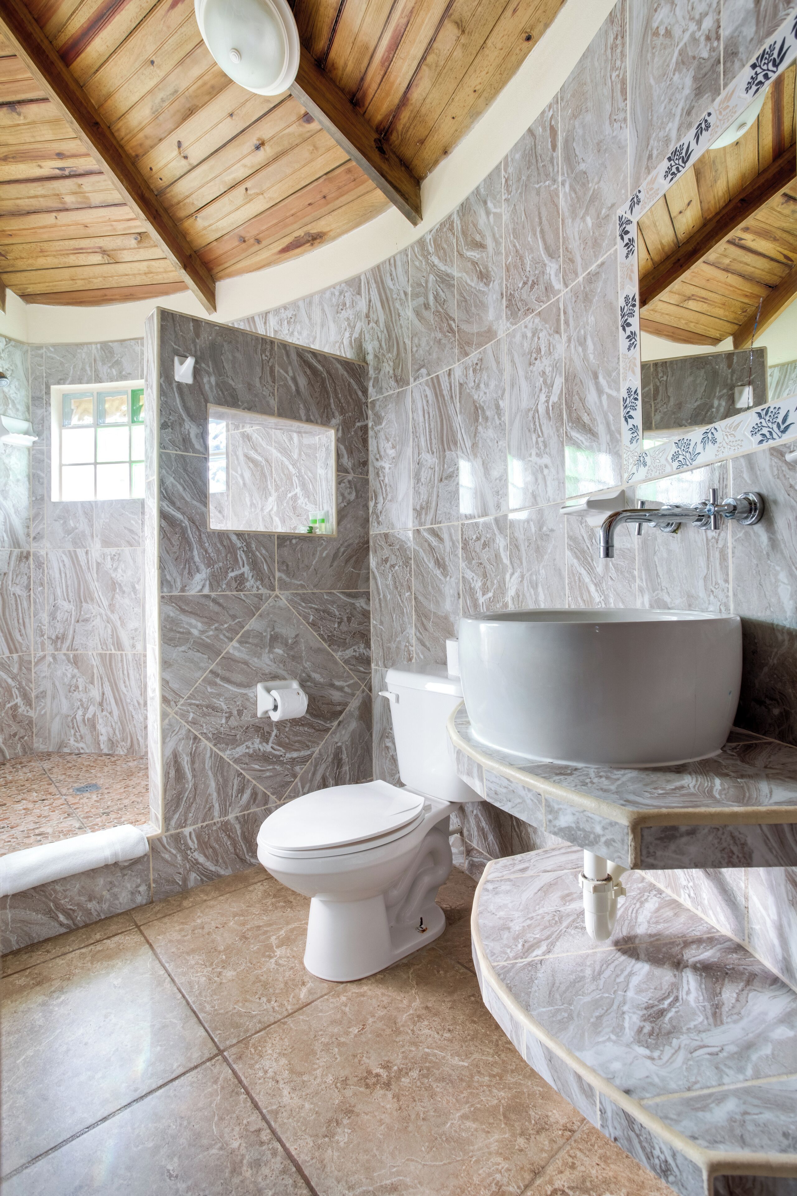 A bathroom with a marble wall, a large sink, a toilet, and a shower area.
