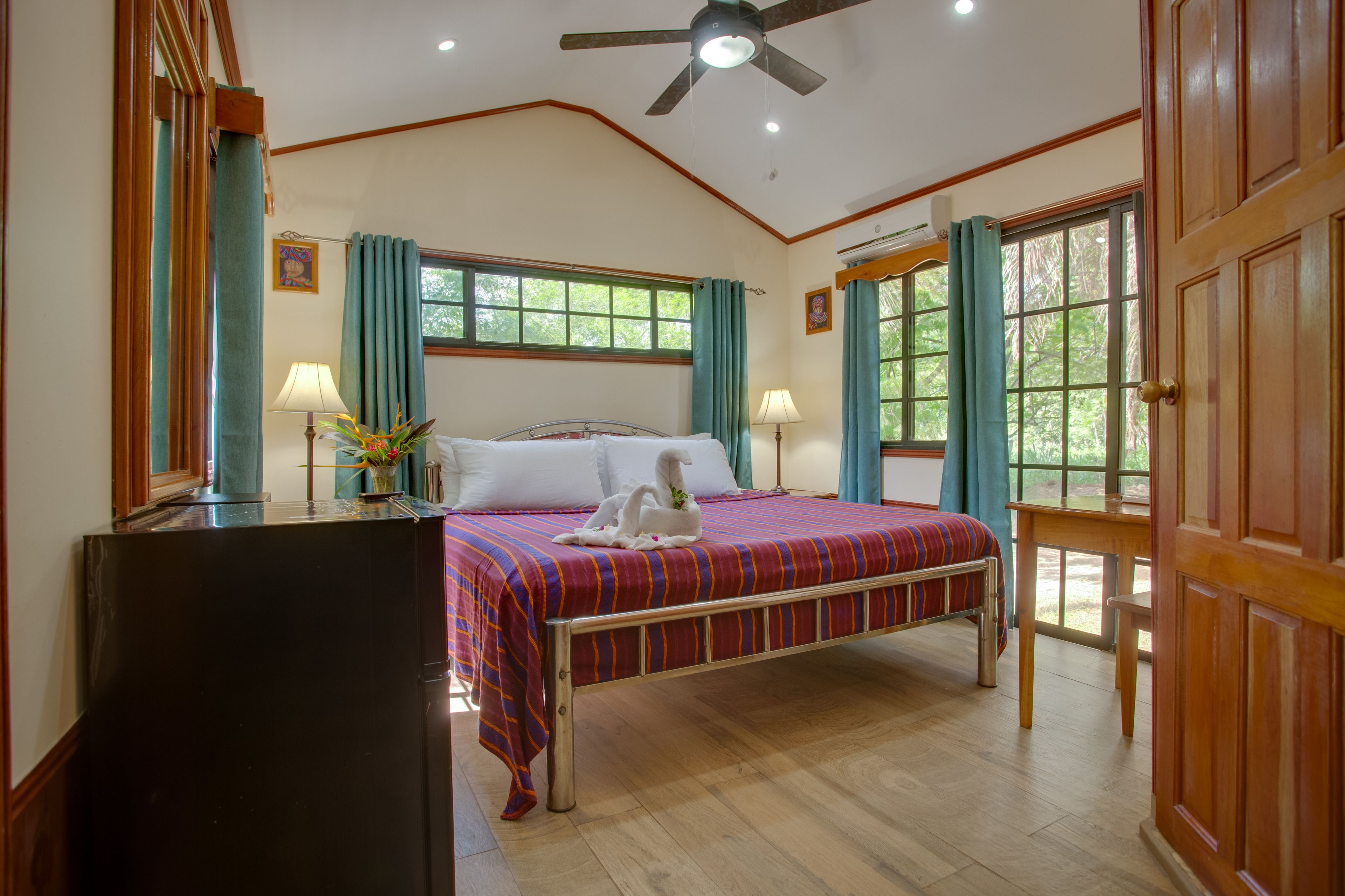 A bedroom with a bed, two bedside lamps, a ceiling fan, and a window with curtains.