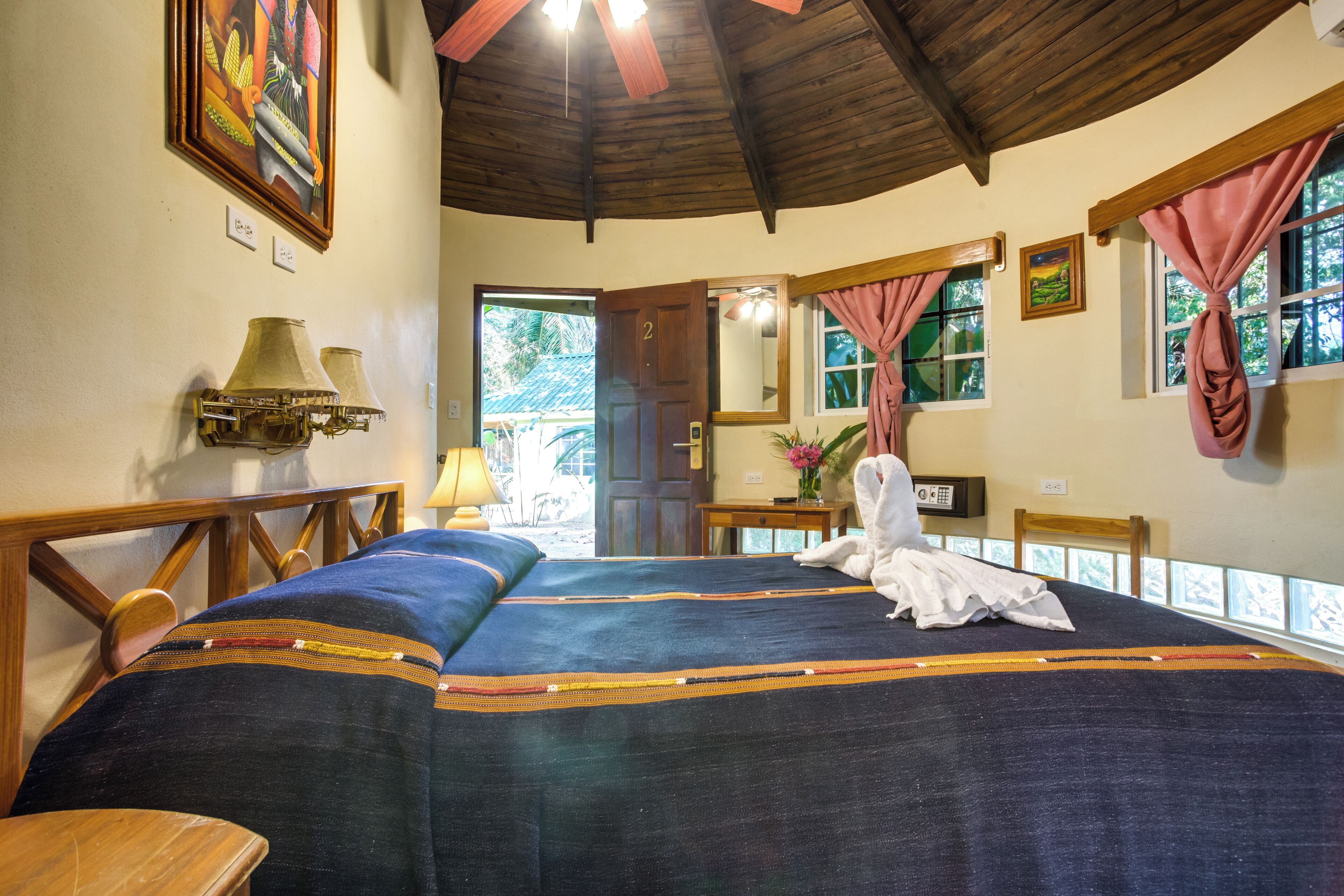 A room with a bed, wooden headboard, a lamp, a painting, and a door leading outside.