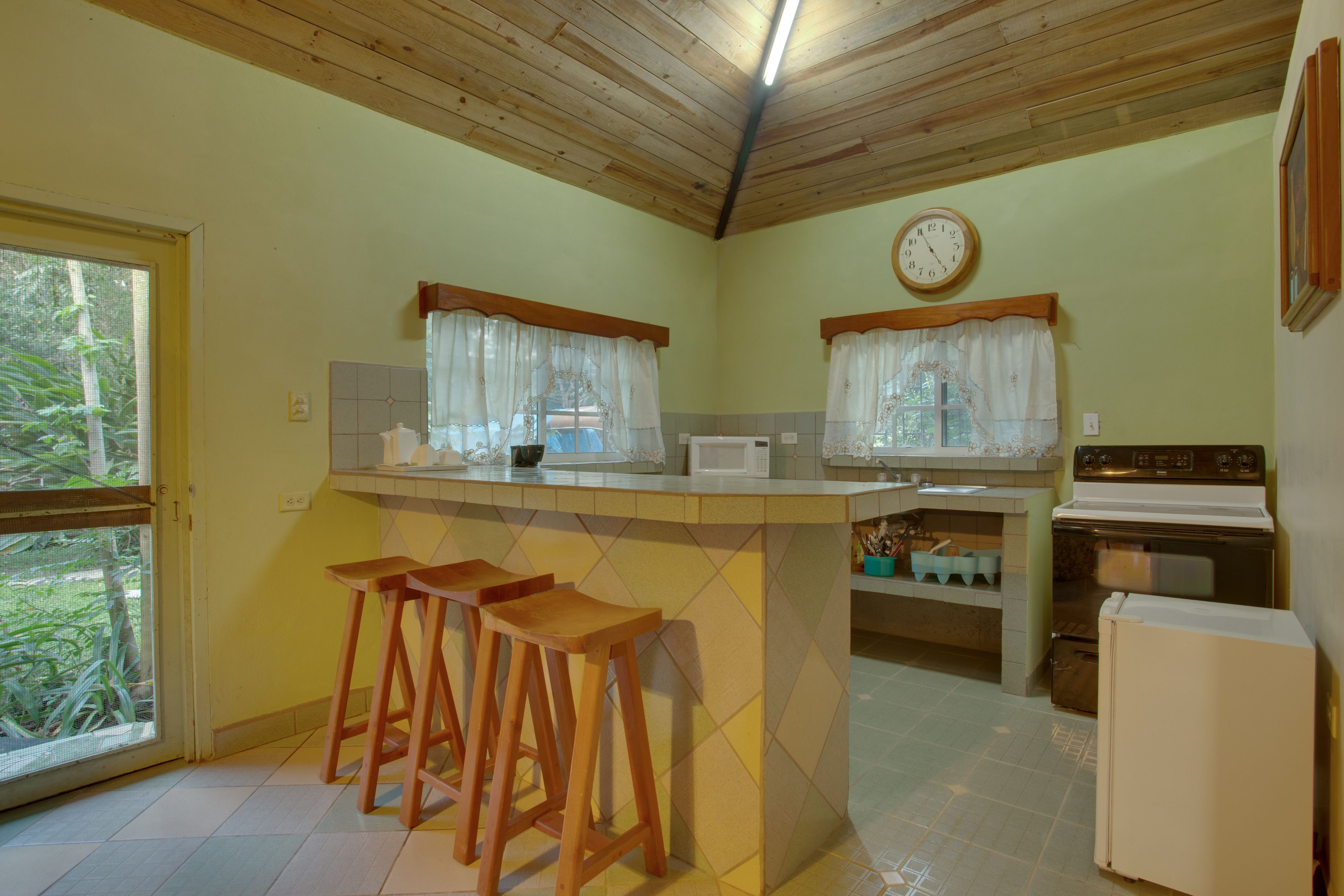 A kitchen with wooden stools, a microwave, a stove, and a refrigerator.