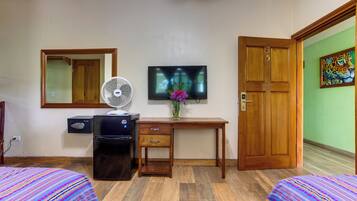 A hotel room with two beds, a desk with a TV, a fan, a refrigerator, and a door with a number.