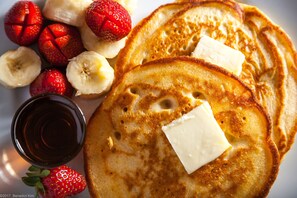 A plate of pancakes with butter and strawberries.