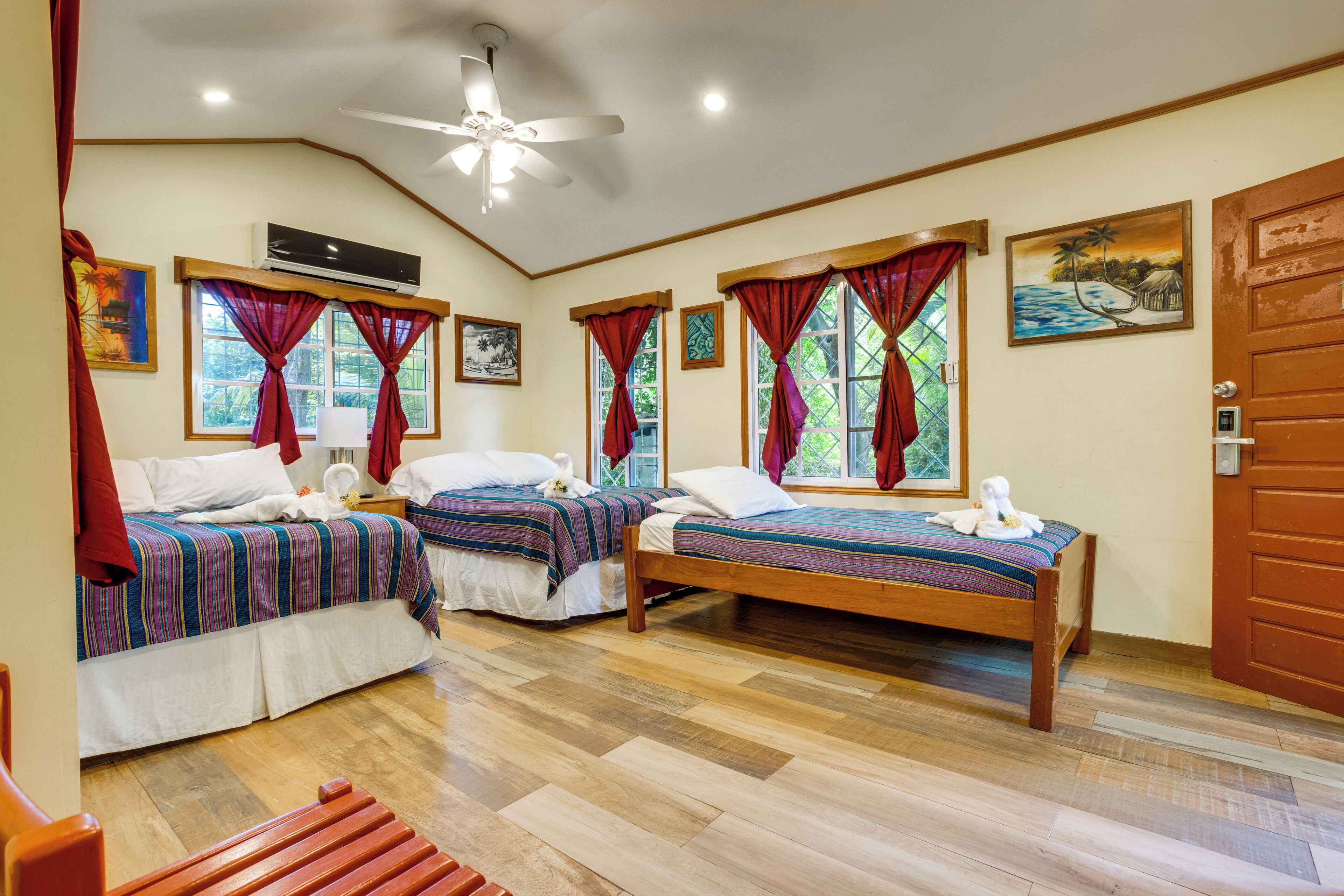 A hotel room with two beds, wooden flooring, a ceiling fan, and artwork on the walls.