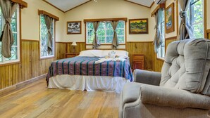 A room with a bed, a chair, wooden walls, and a ceiling fan.