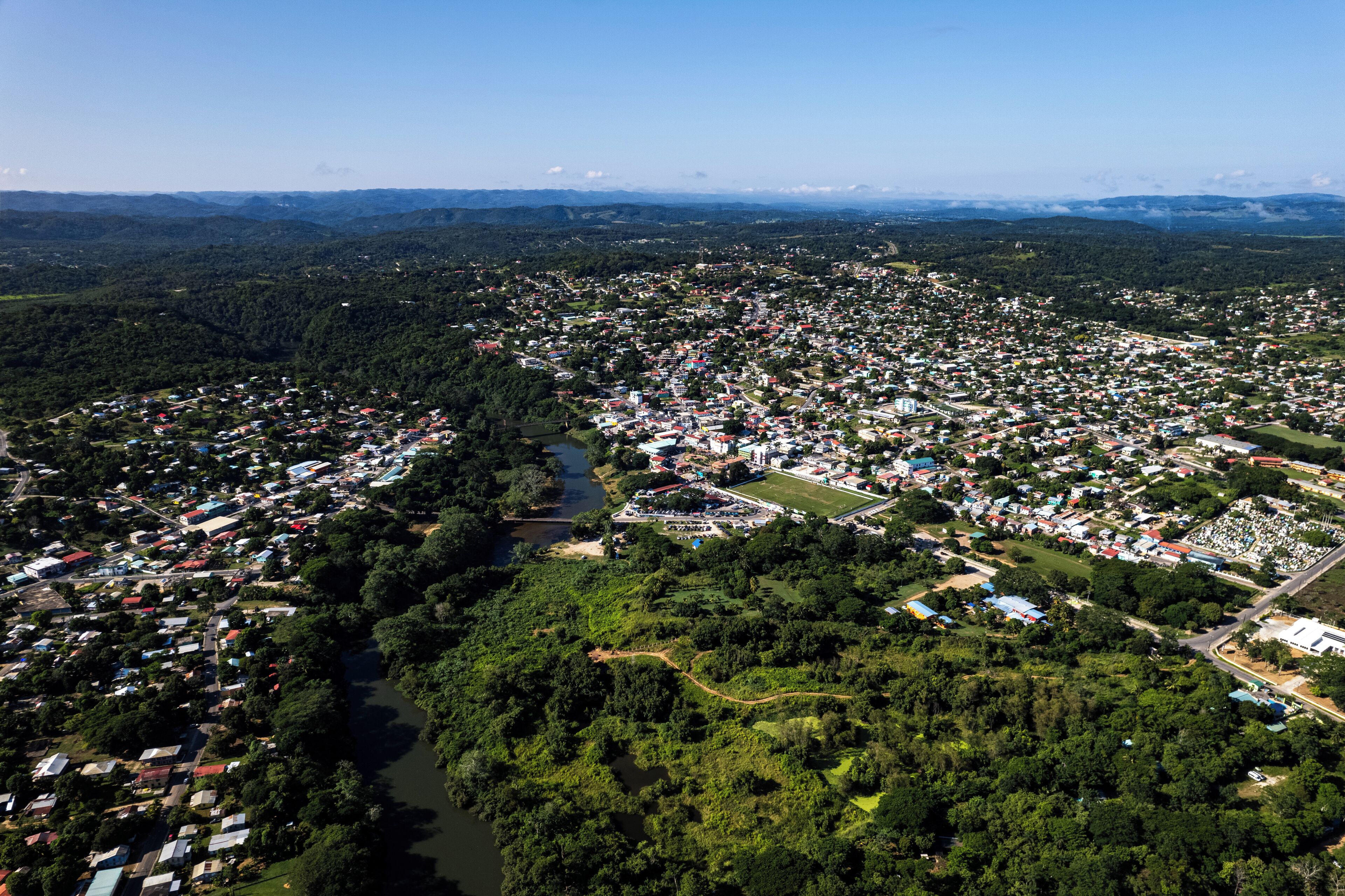 An aerial view of a town with a river running through it, surrounded by dense forests and residential areas.