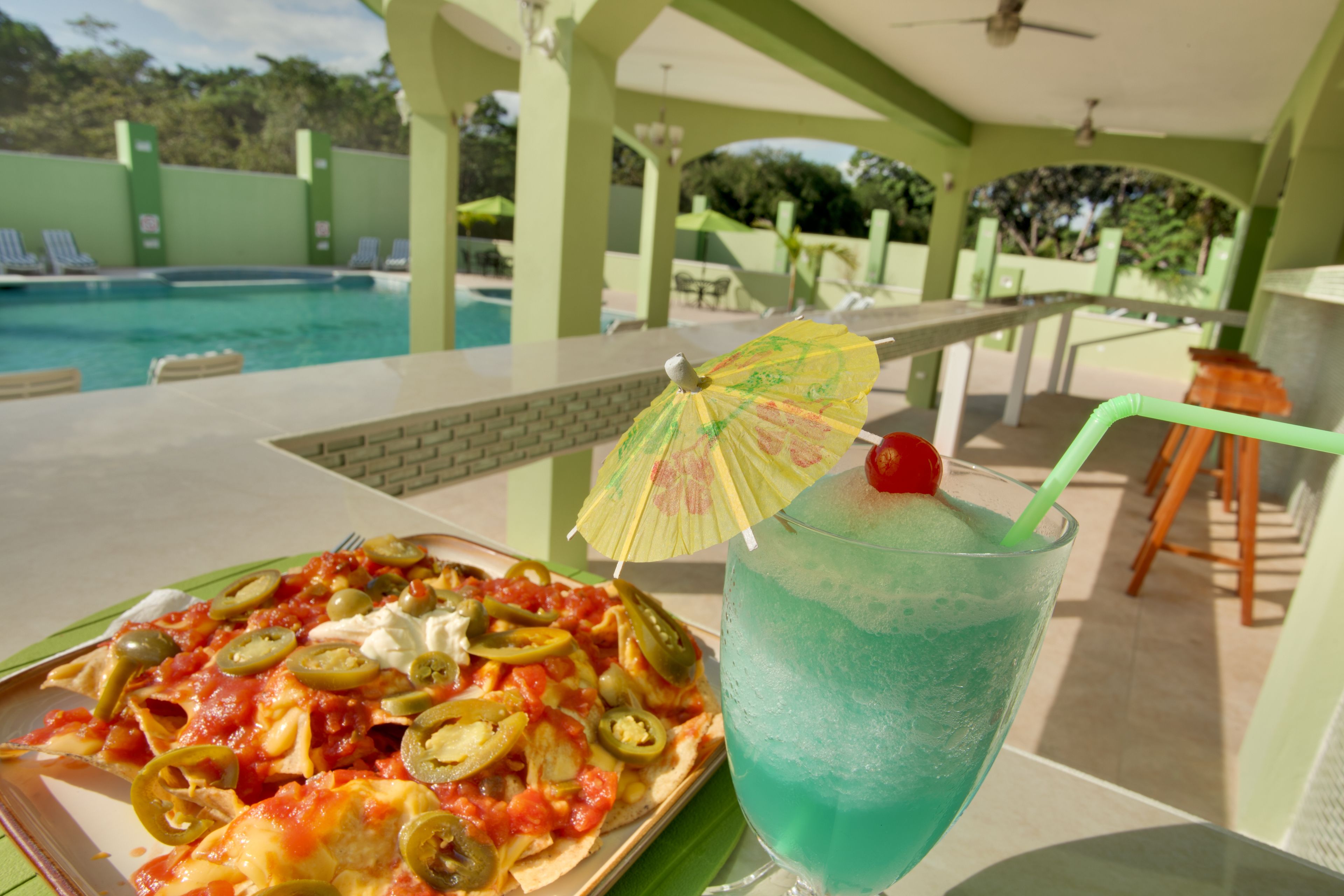 A dining table with a plate of nachos and a blue drink with a straw and umbrella.