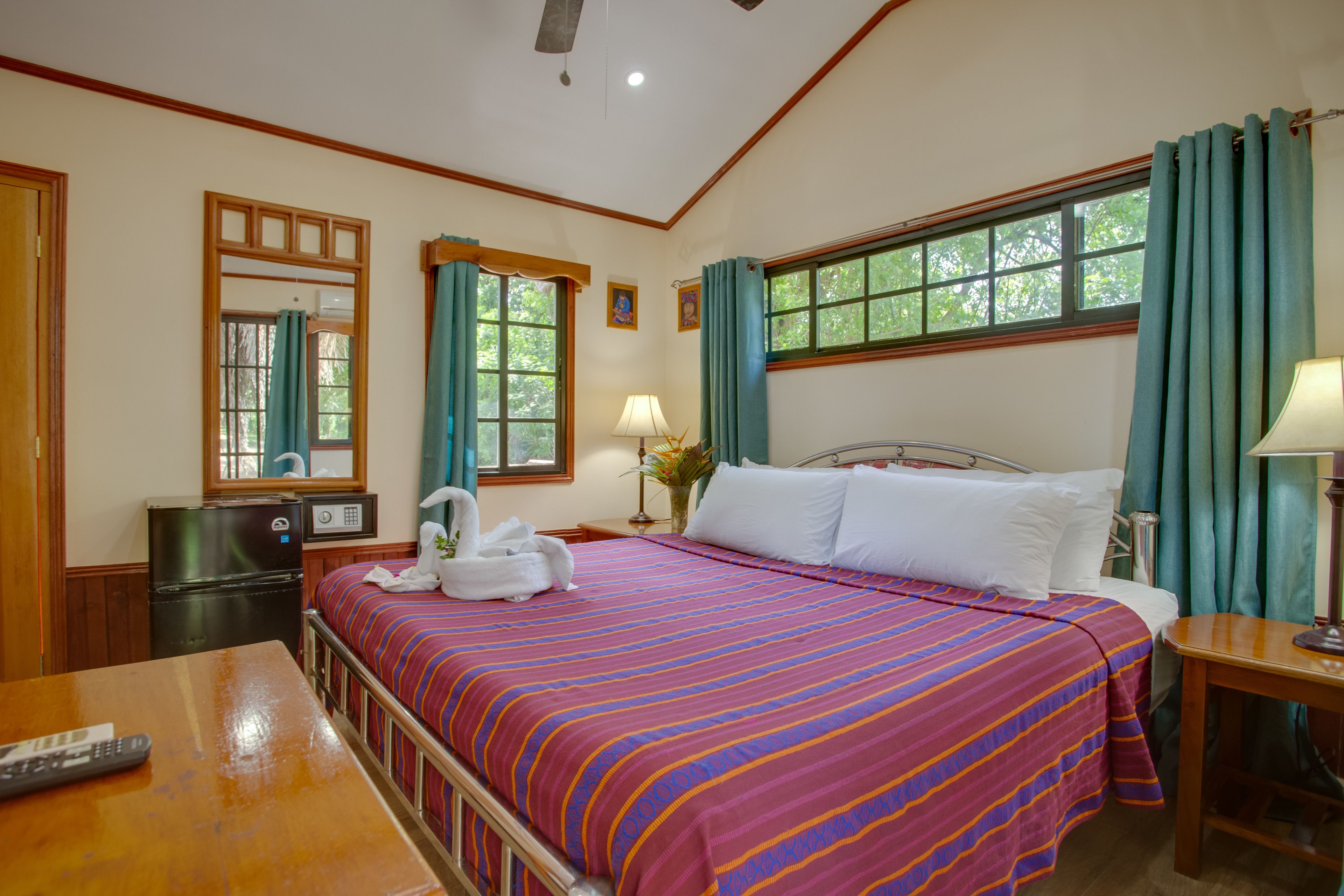 A hotel room with a bed, a desk, a refrigerator, and a window with curtains.