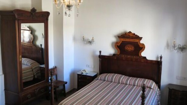 Un dormitorio con cama de madera, un espejo grande, una araña y una mesita de noche.