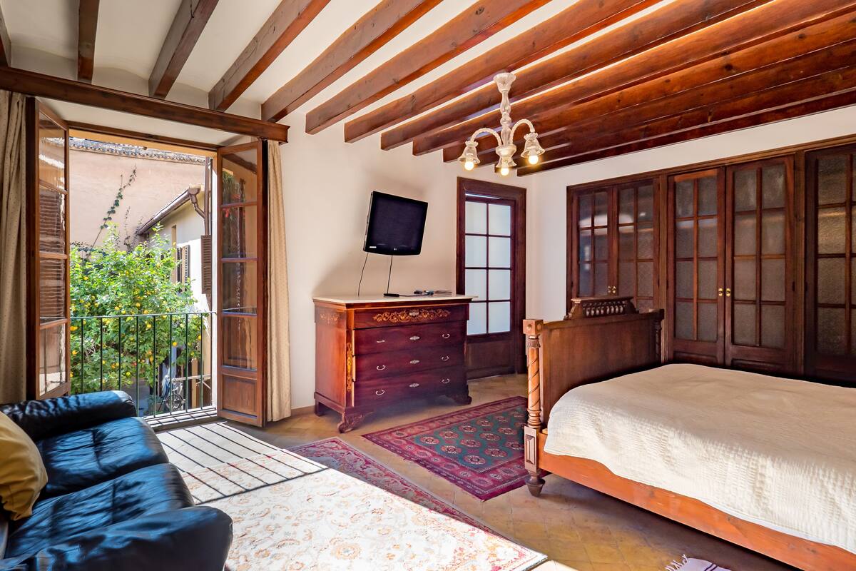 A bedroom with a wooden ceiling, a bed, a dresser, a television, and a view of the outside.