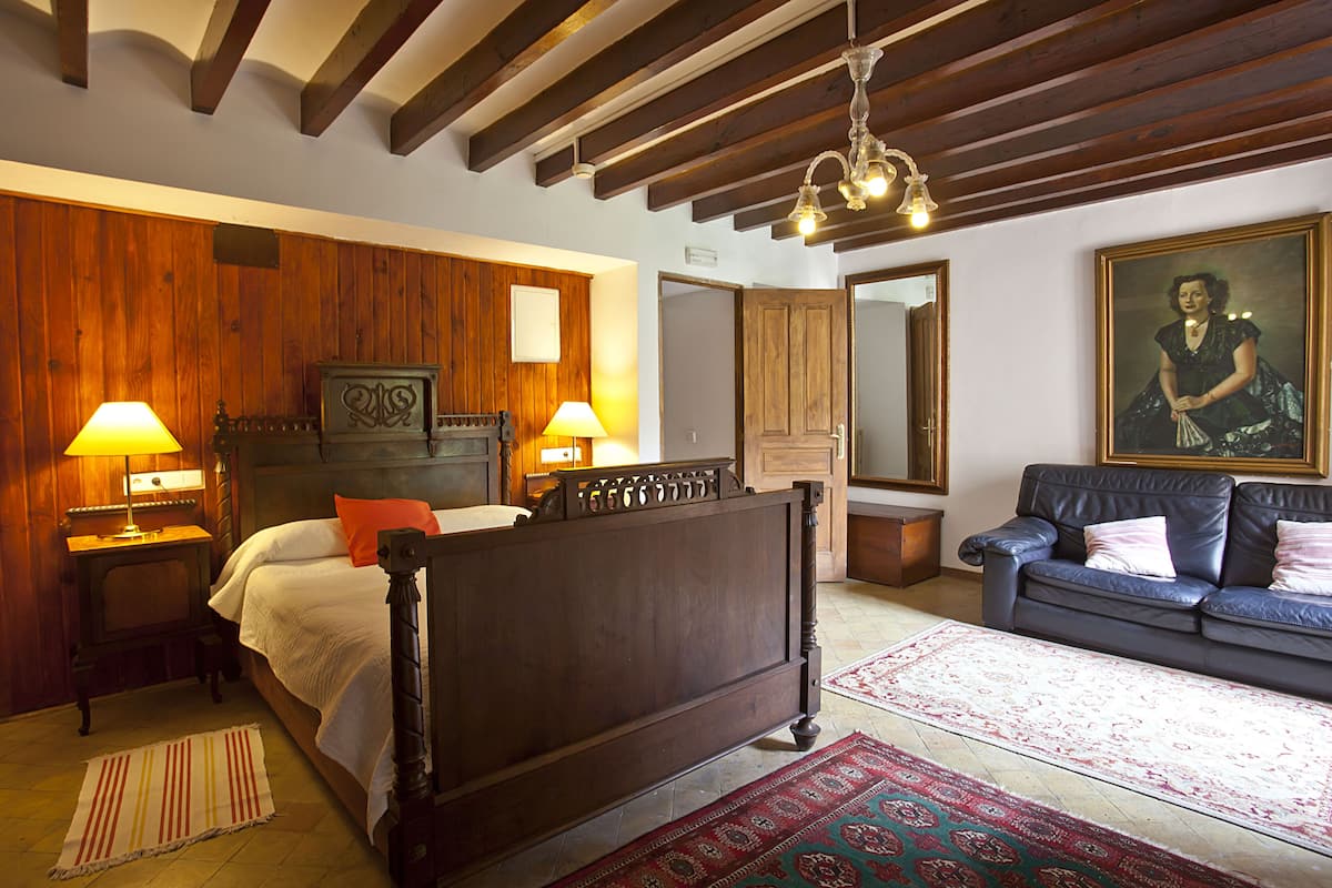 A bedroom with a wooden bed, a sofa, a rug, and a painting.