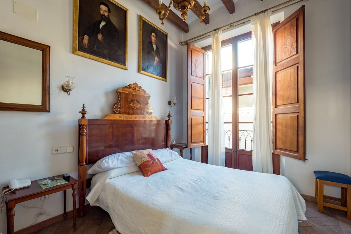 A bedroom with a wooden bed, a nightstand, a bedside table, and a window with curtains.