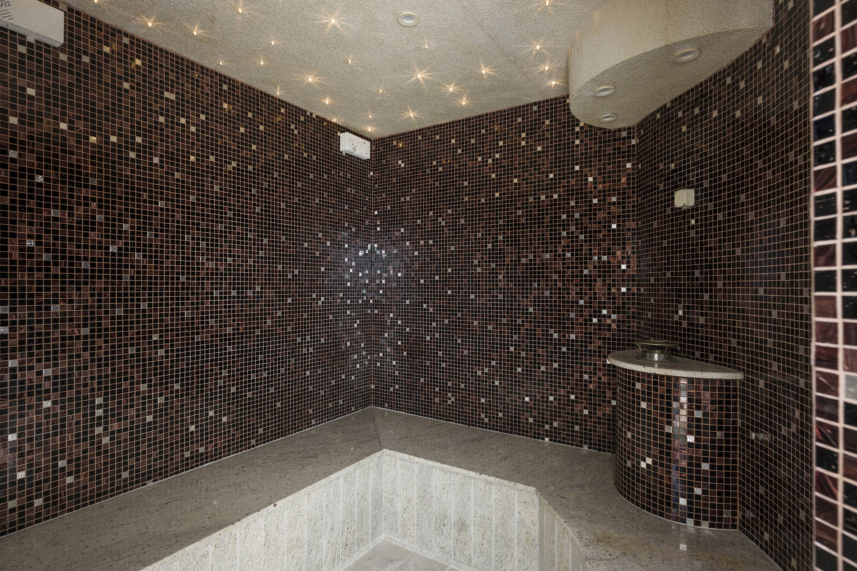 A modern bathroom with mosaic tile walls, a central sink, and a built-in bathtub.