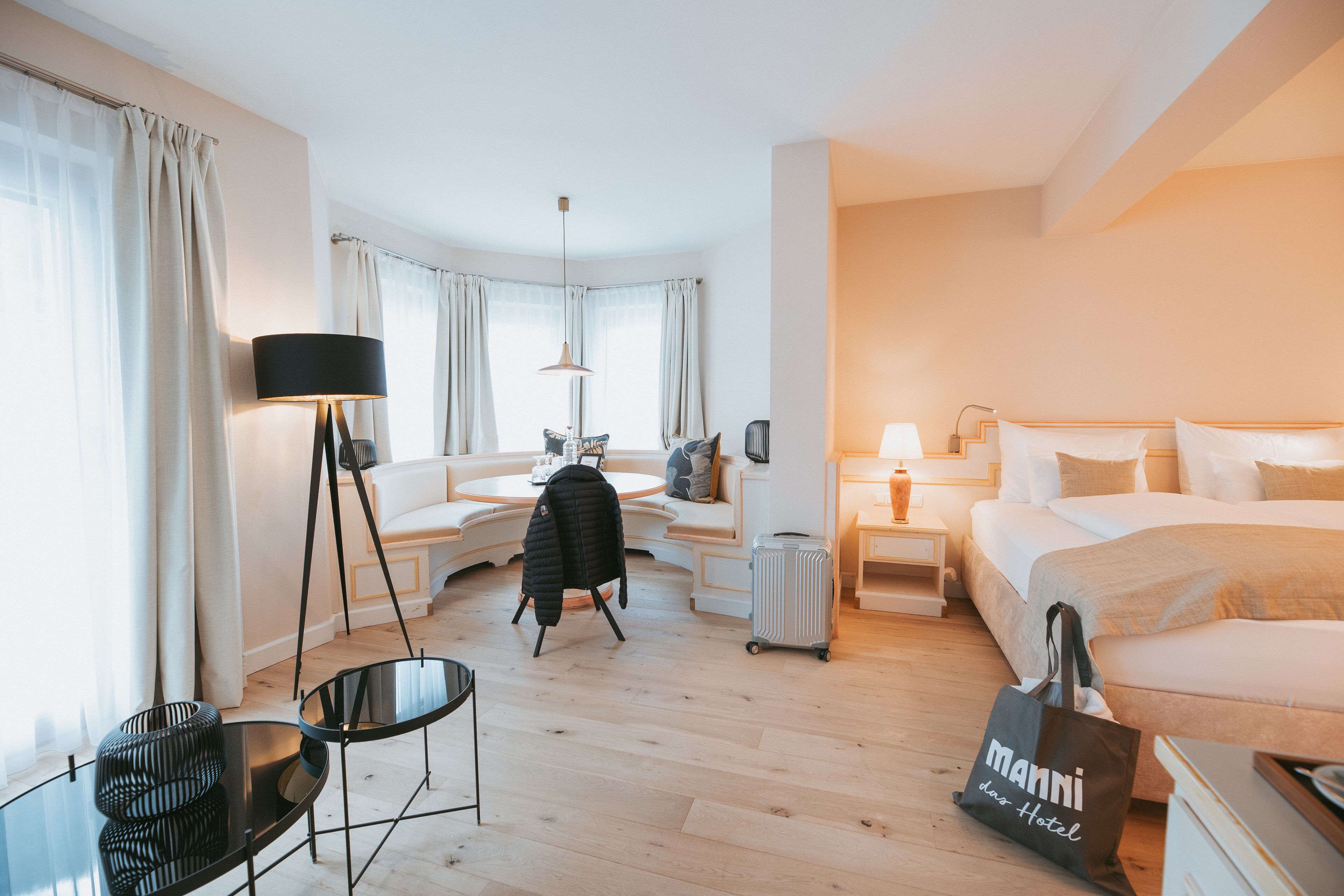 A hotel room with a bed, a sofa, a desk, a chair, a lamp, and a suitcase.