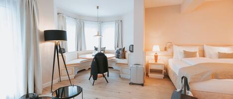 A hotel room with a bed, a sofa, a desk, a chair, a lamp, and a suitcase.