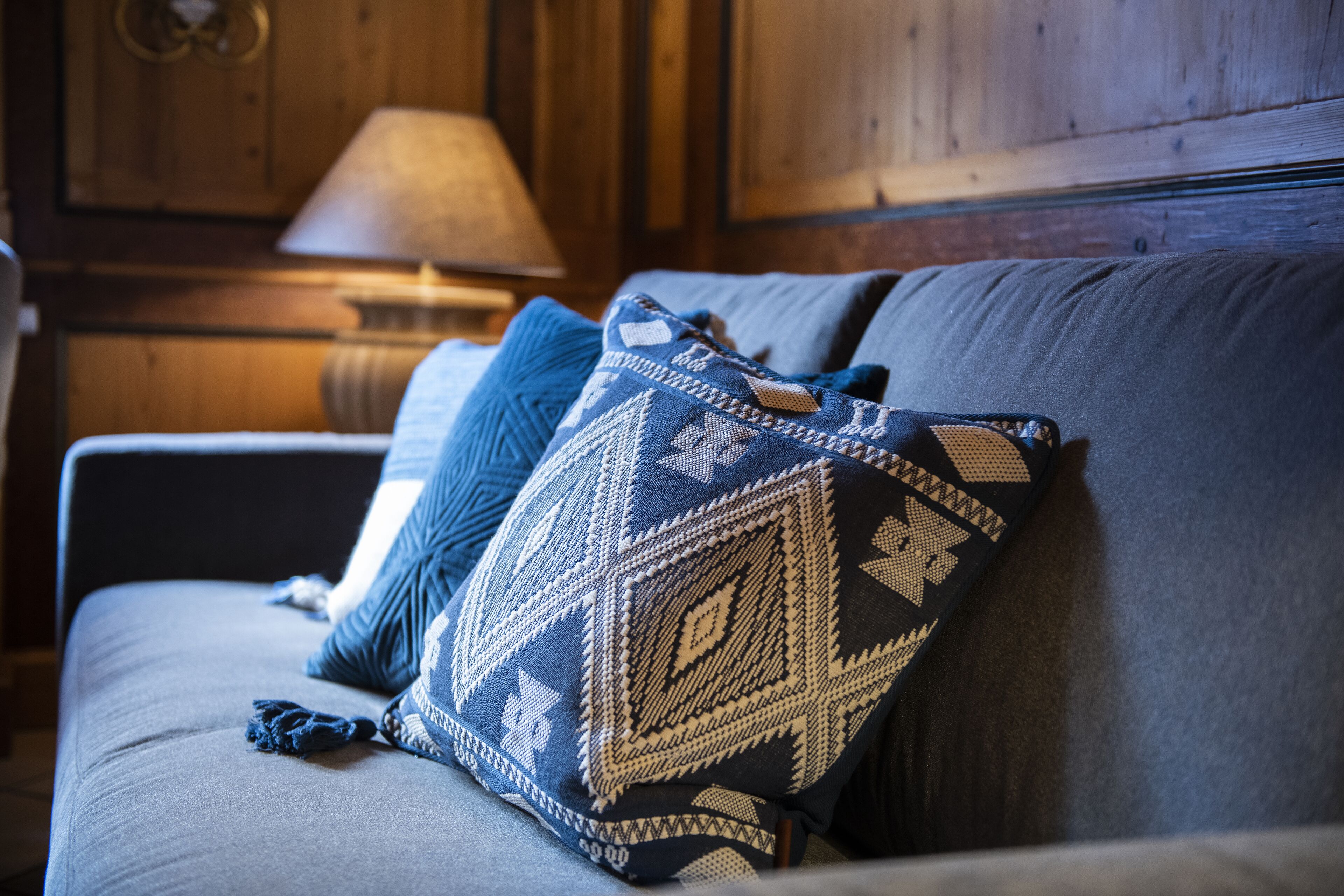 A sofa with patterned cushions and a lamp in the background.