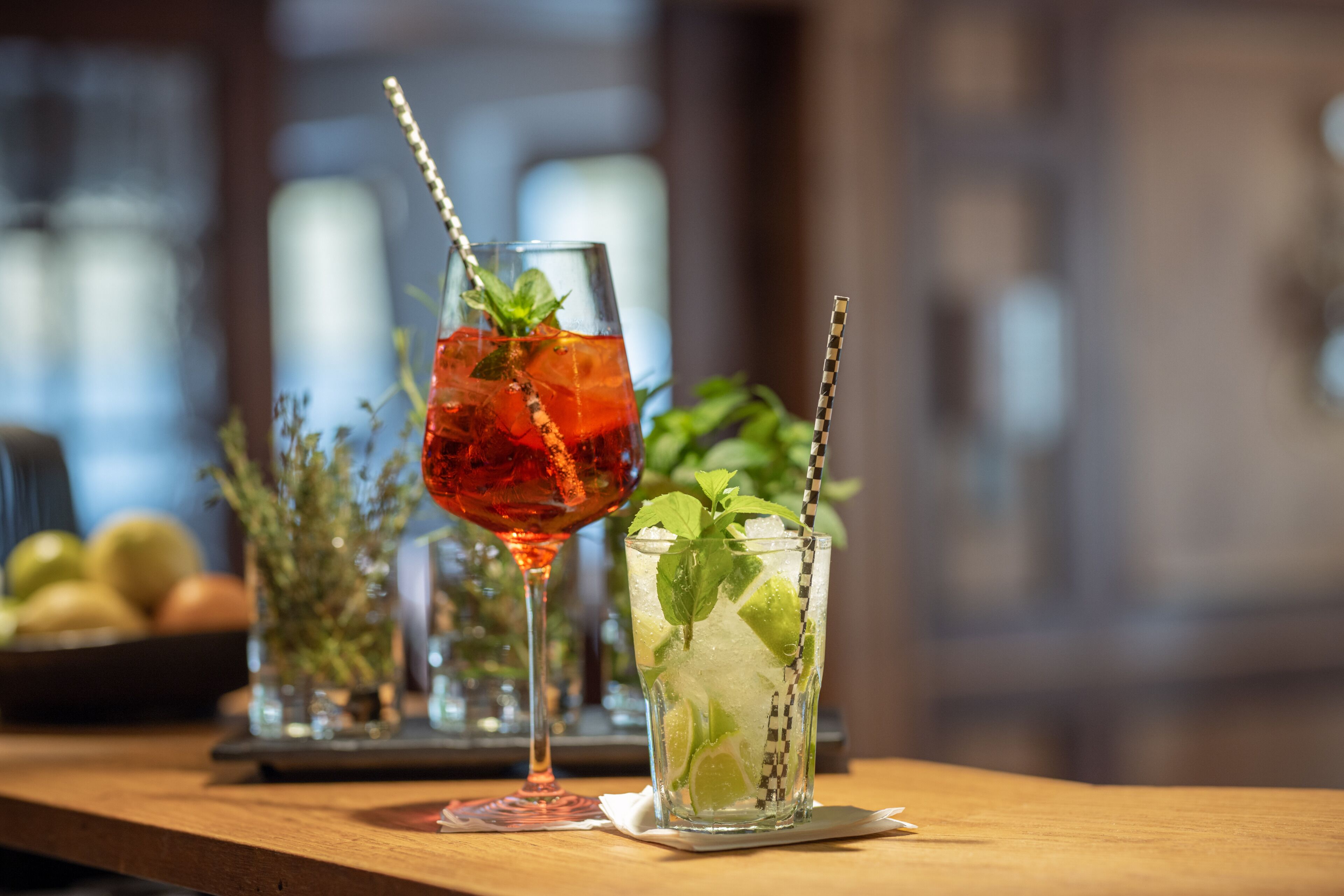 Two glasses of cocktails on a wooden bar counter with a blurred background.