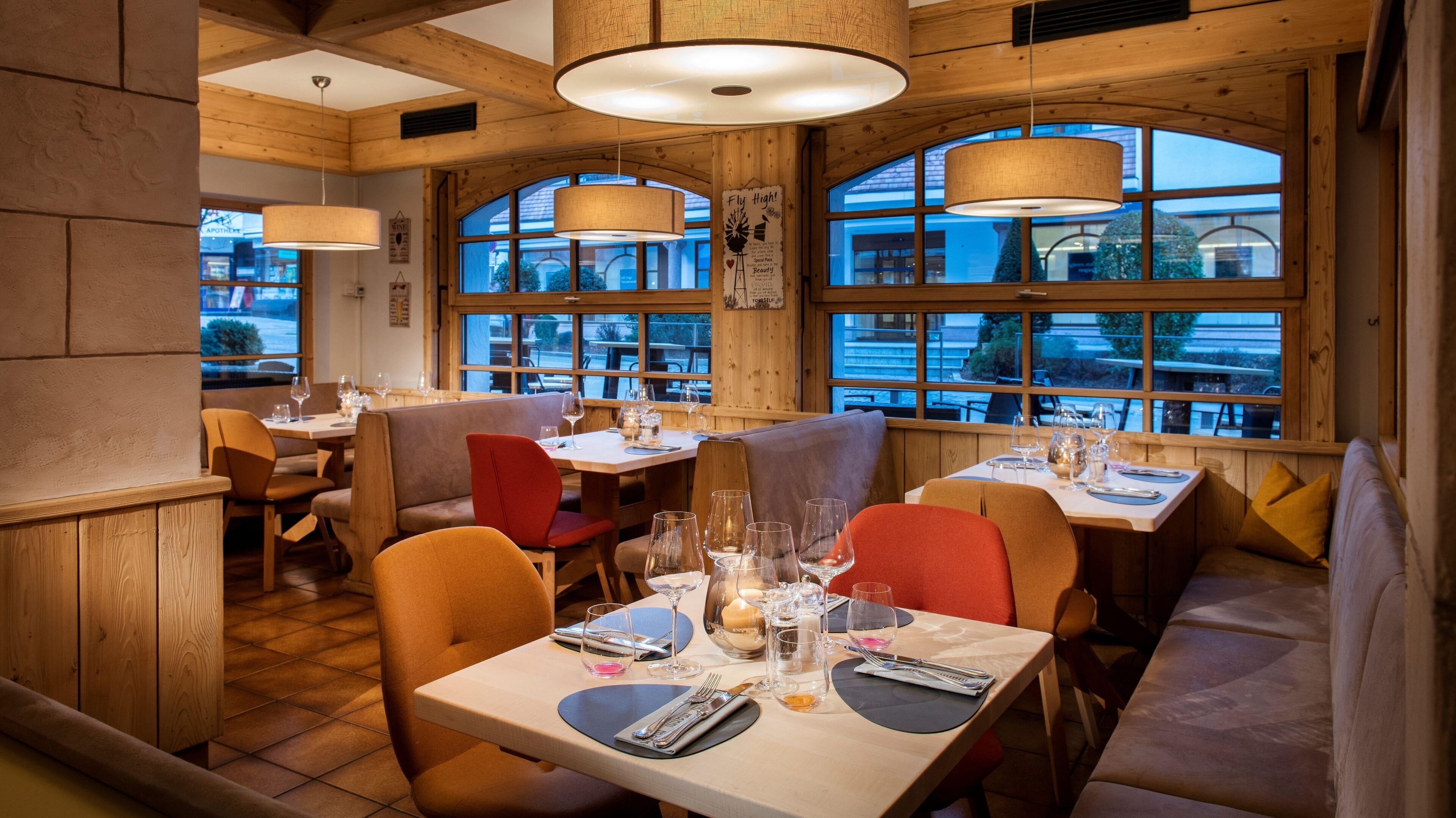 Interior de restaurante con vigas de madera, amplias ventanas y un ambiente acogedor. Mesas preparadas con copas de vino y cubiertos.