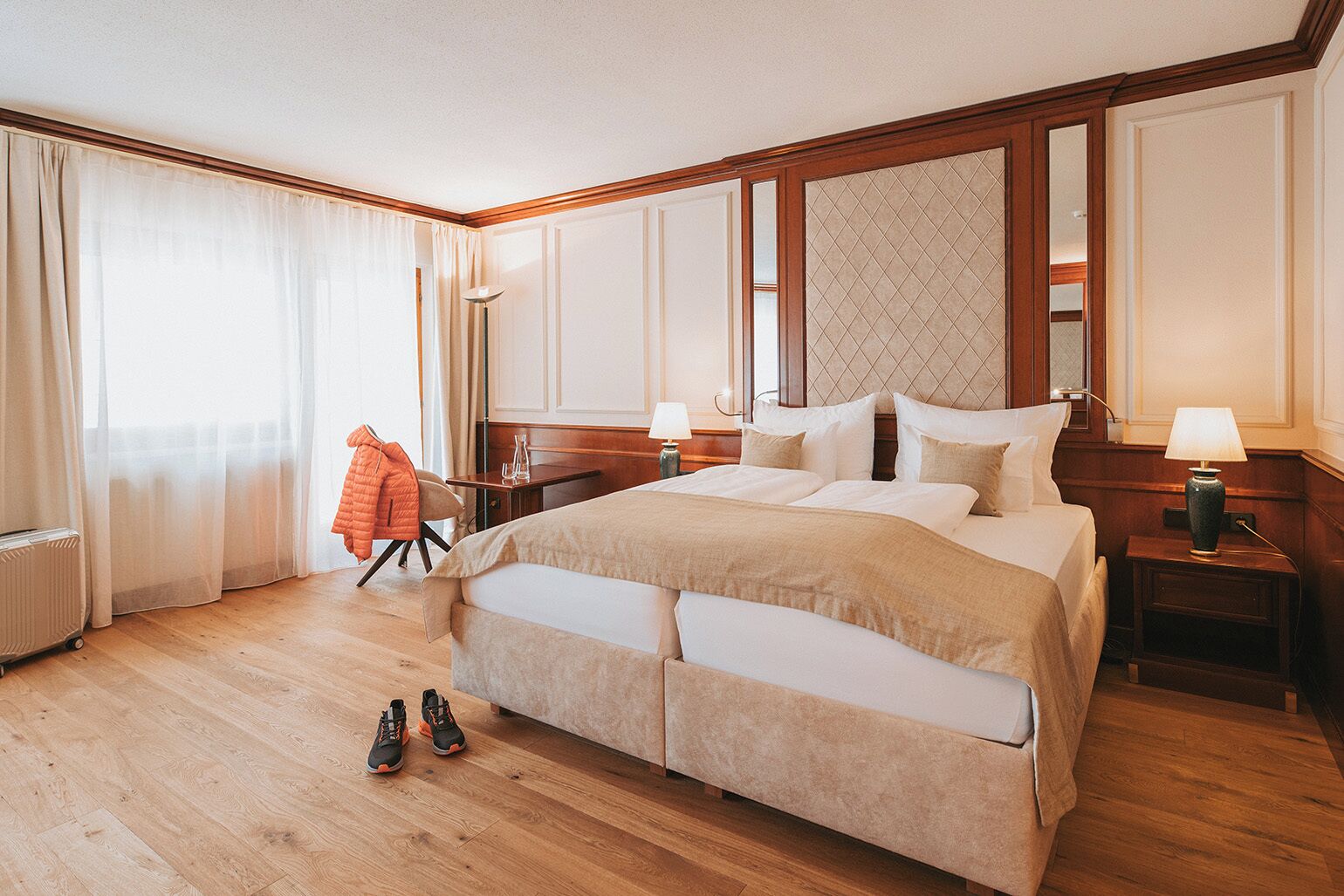 Une chambre d’hôtel spacieuse, dotée d’un grand lit, d’un plancher en bois, d’une chaise et d’une table de chevet avec une lampe.