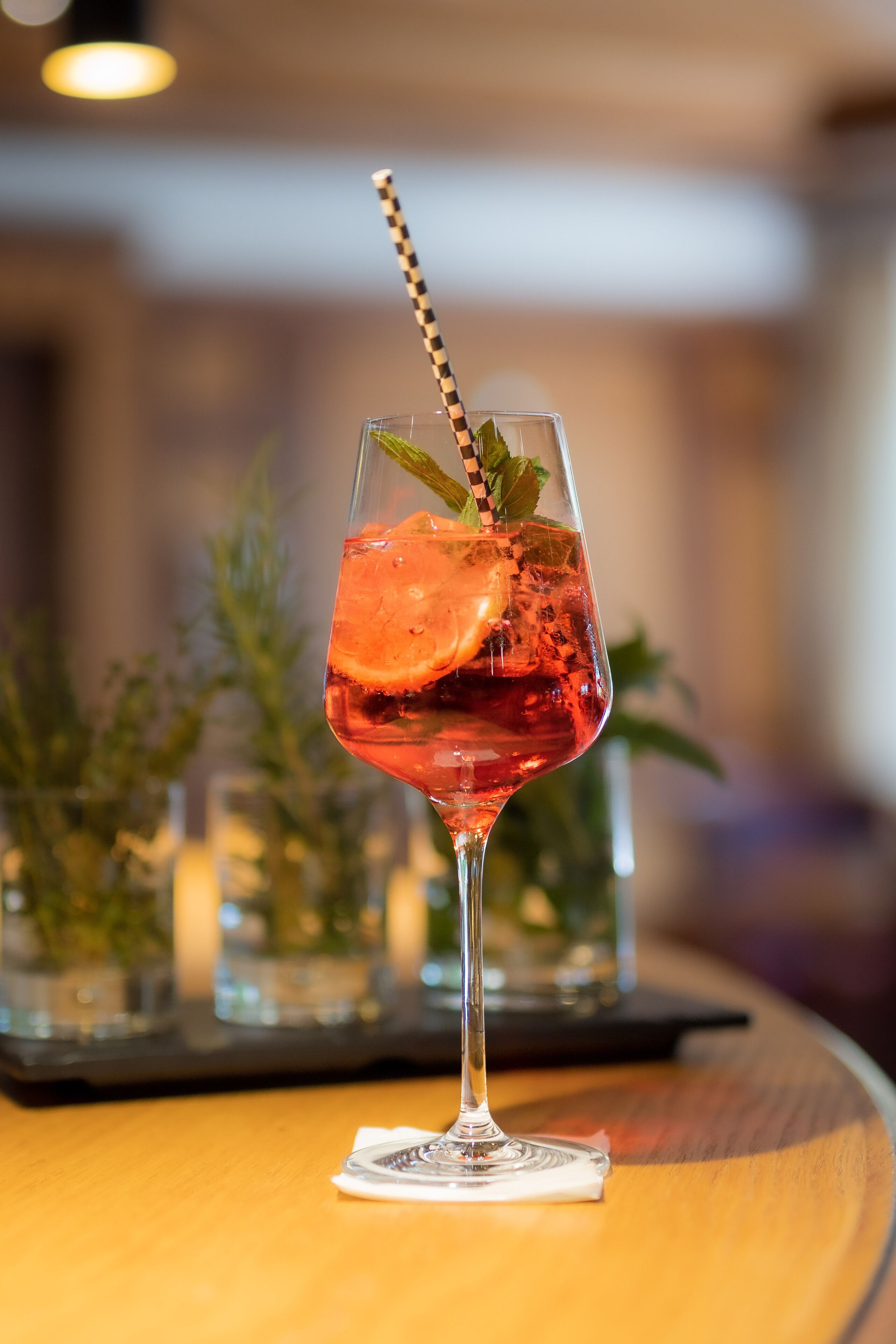 A cocktail glass with a striped straw, garnished with a mint leaf, on a wooden table.