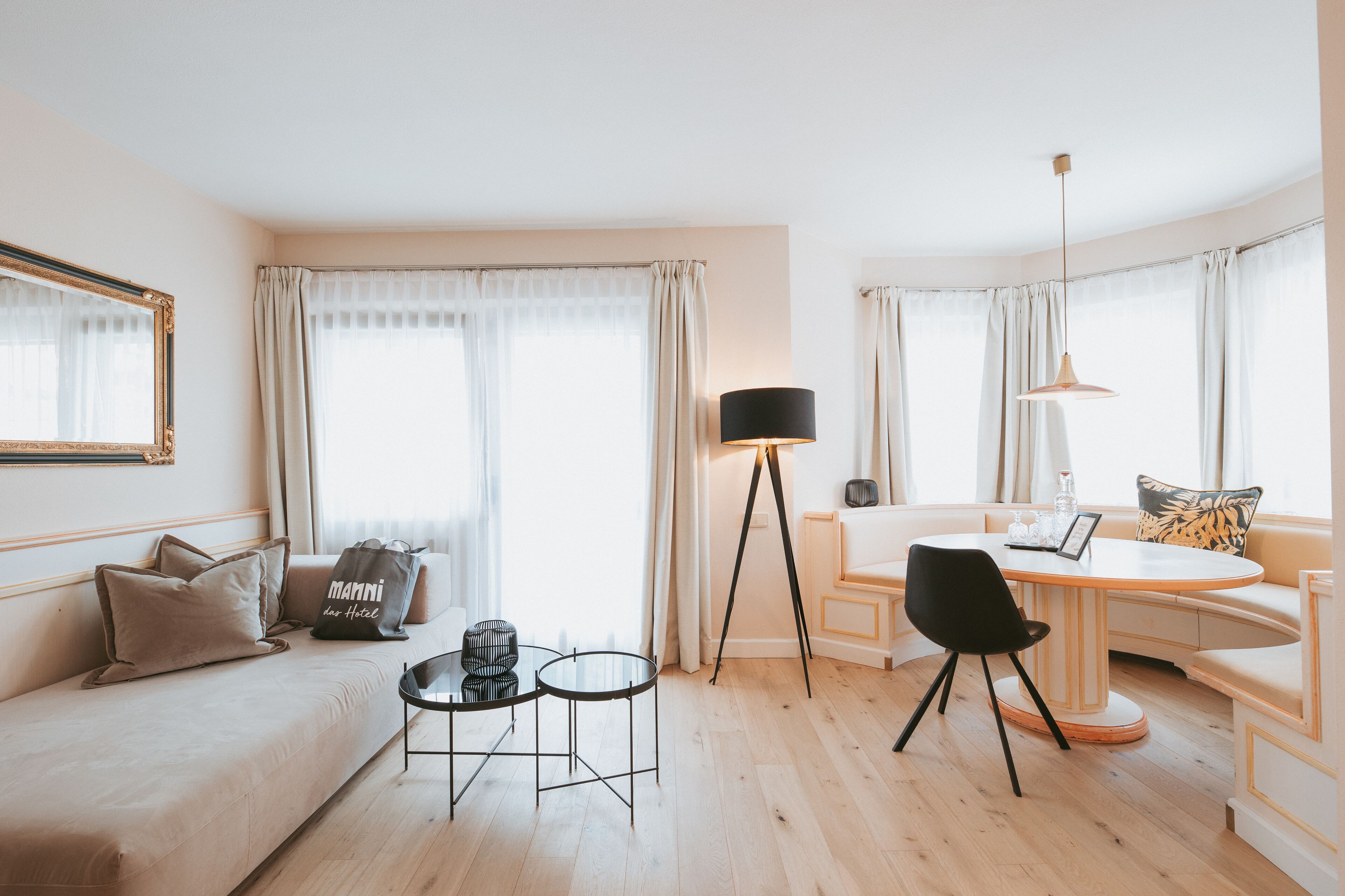 Una habitación de hotel moderna con un sofá, dos mesitas, una mesa de comedor y una lámpara de pie.