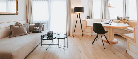 Una habitación de hotel moderna con un sofá, dos mesitas, una mesa de comedor y una lámpara de pie.