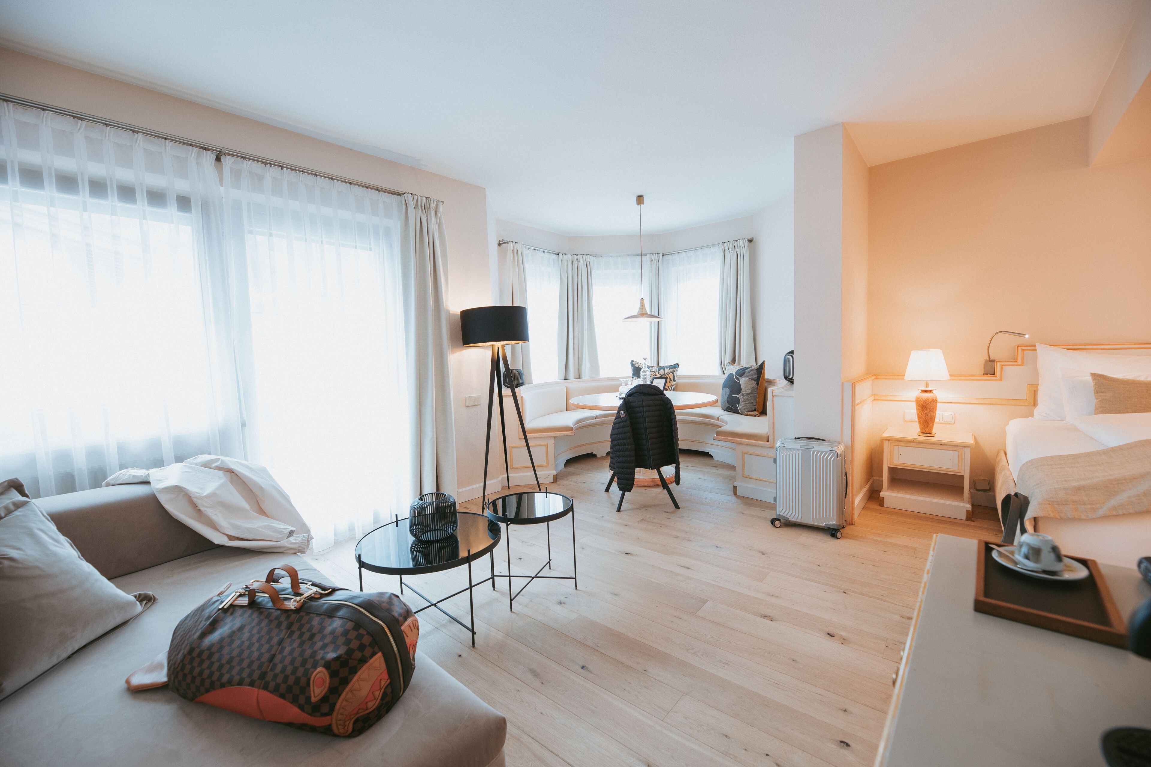 A hotel room with a sofa, a small table, a lamp, a bed, and a suitcase.