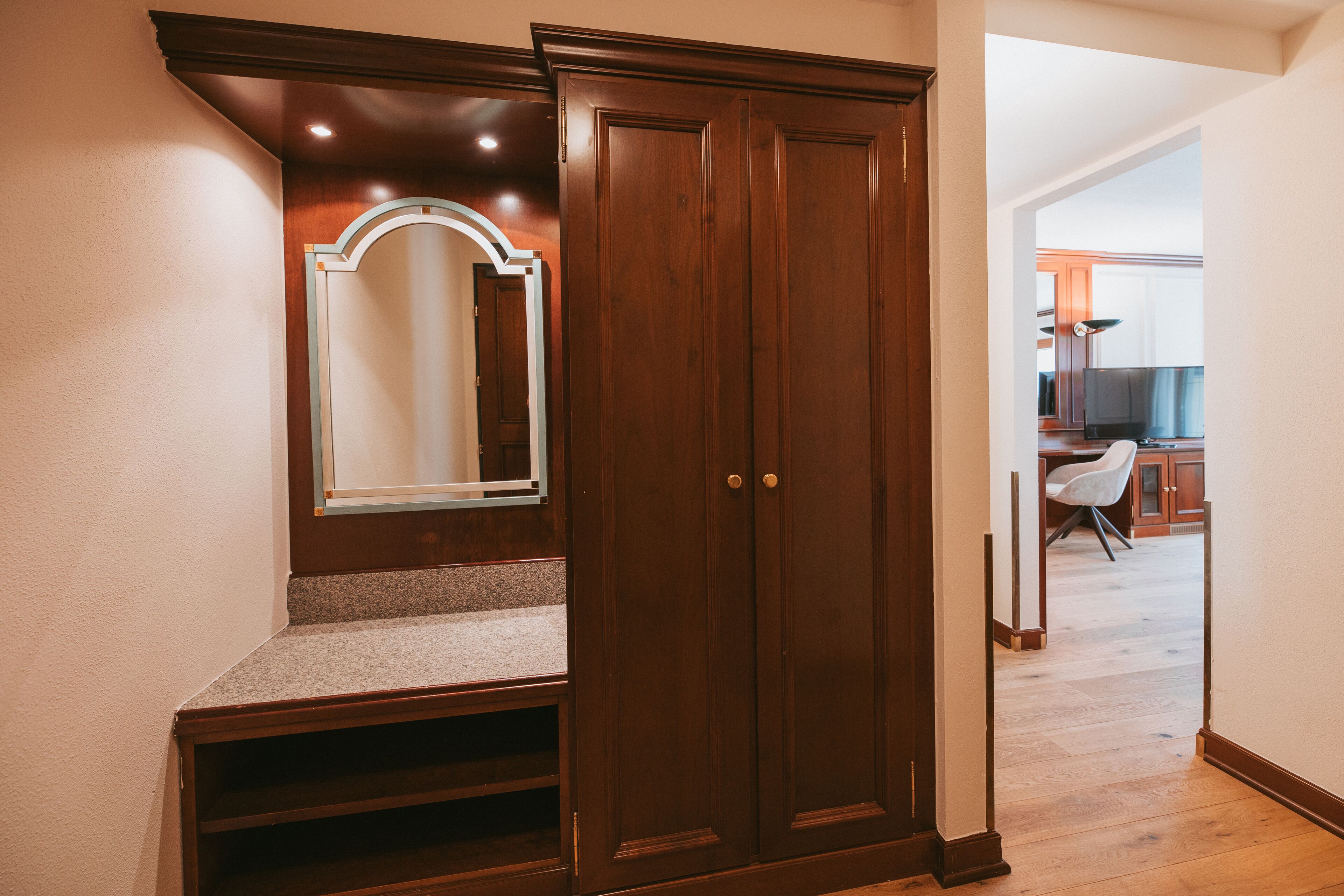 Un couloir avec une armoire en bois, un miroir et un escalier menant à une autre pièce.