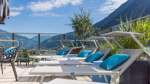 A terrace with sun loungers and a table, overlooking a mountainous landscape. - MANNI The Hotel (Mayrhofen)
