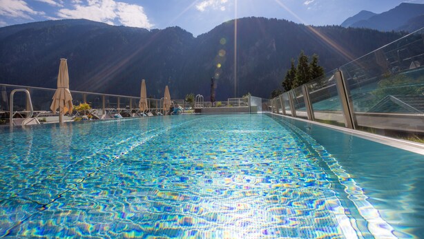 A swimming pool with clear water, surrounded by lounge chairs and umbrellas, with mountains in the background. - MANNI The Hotel (Mayrhofen)