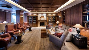A spacious lounge area with wooden flooring, plush seating, a fireplace, and a wine rack. - MANNI The Hotel (Mayrhofen)