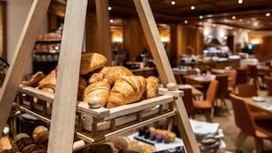 A bakery display with various pastries and bread, wooden furniture, and a dining area with tables and chairs. - MANNI The Hotel (Mayrhofen)