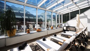 A sunlit room with large windows, a potted plant, lounge chairs, and a table. - MANNI The Hotel (Mayrhofen)