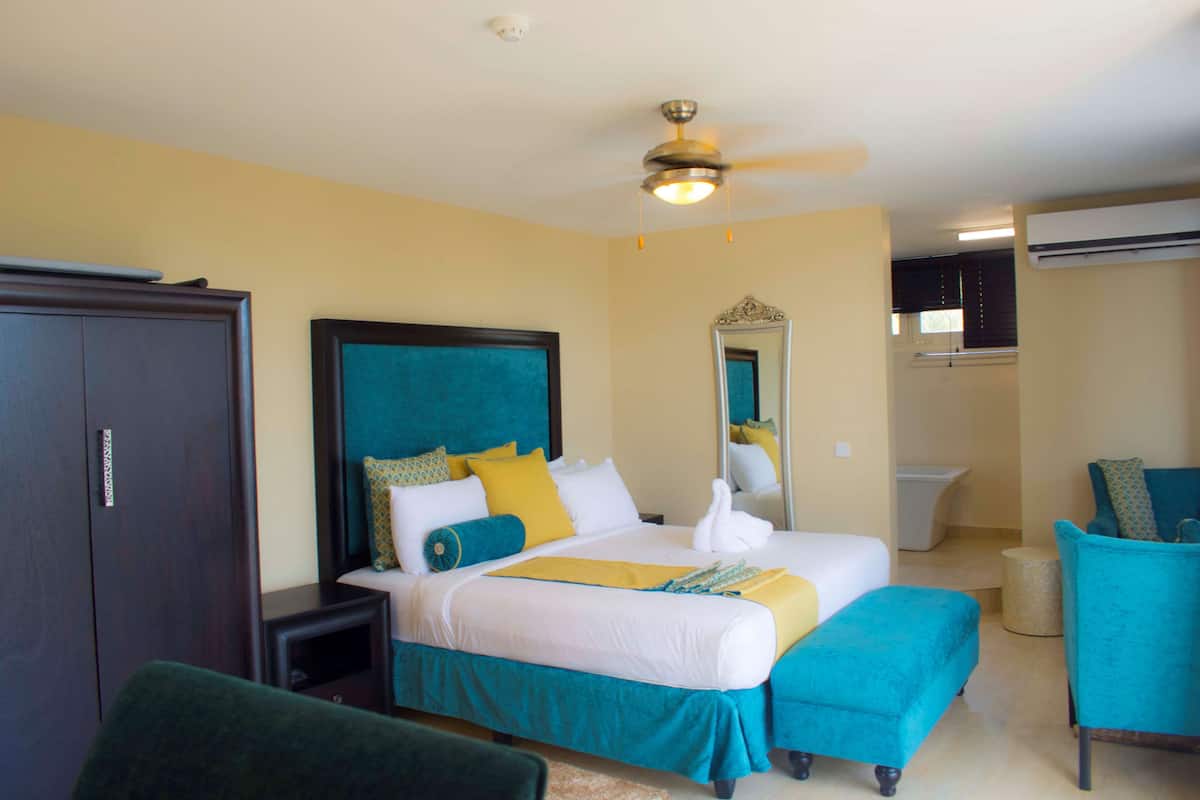 A hotel room with a bed, a chair, a wardrobe, a mirror, and an air conditioning unit.
