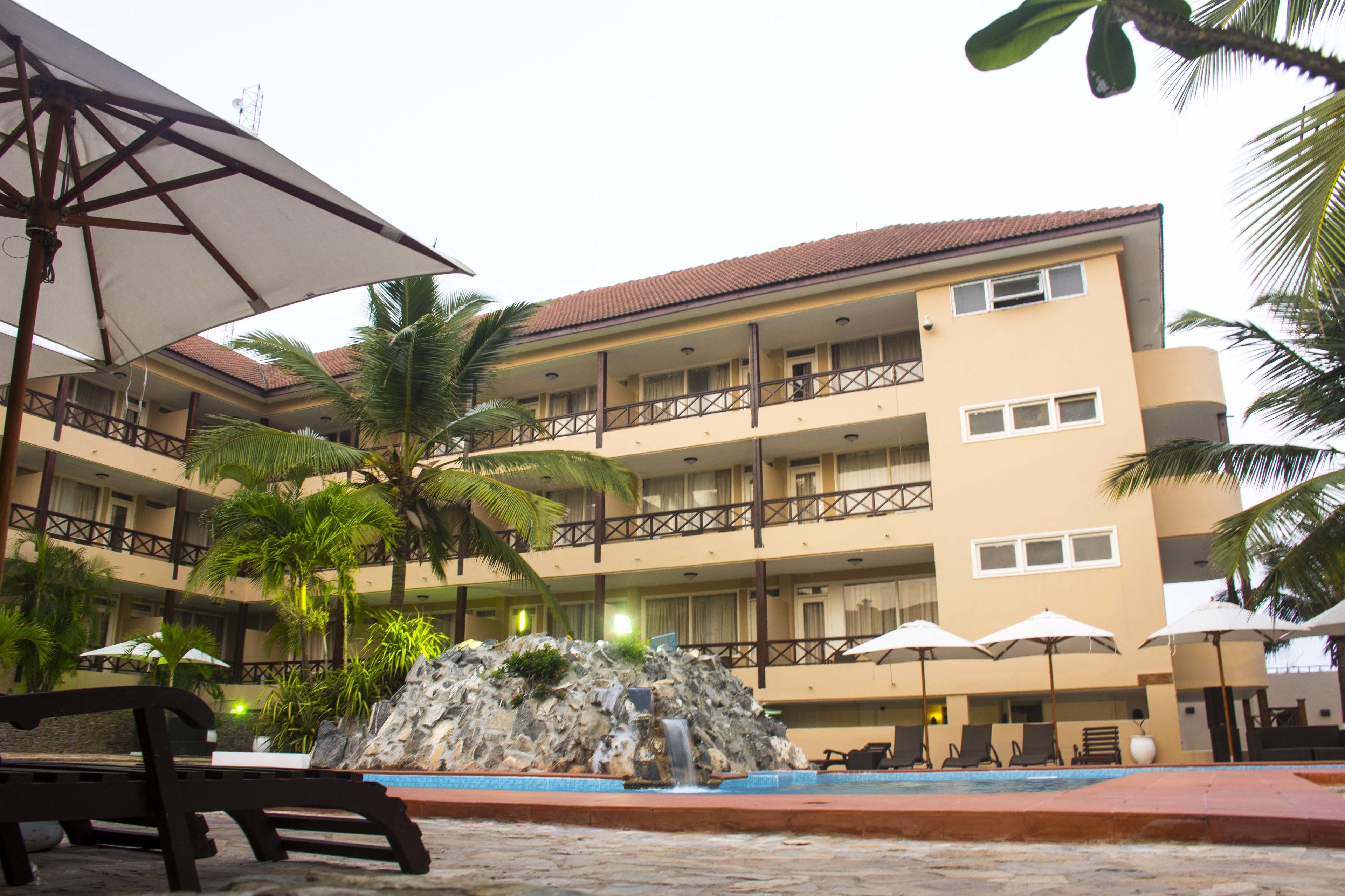 A hotel with a pool, palm trees, and a waterfall feature.