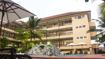 A hotel with a pool, palm trees, and a waterfall feature.