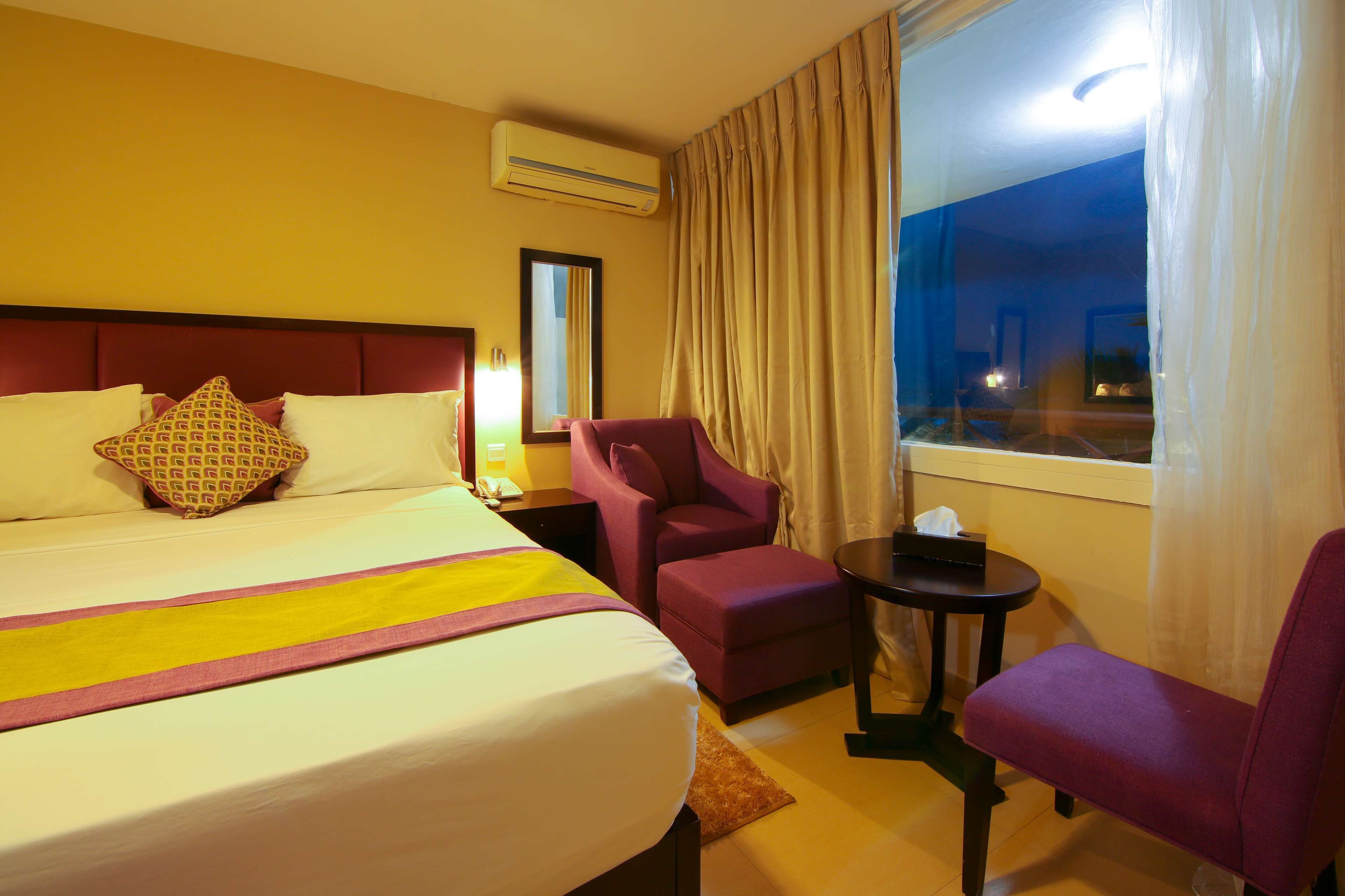 Una habitación de hotel con una cama grande, una silla, una mesita y una ventana con cortinas.