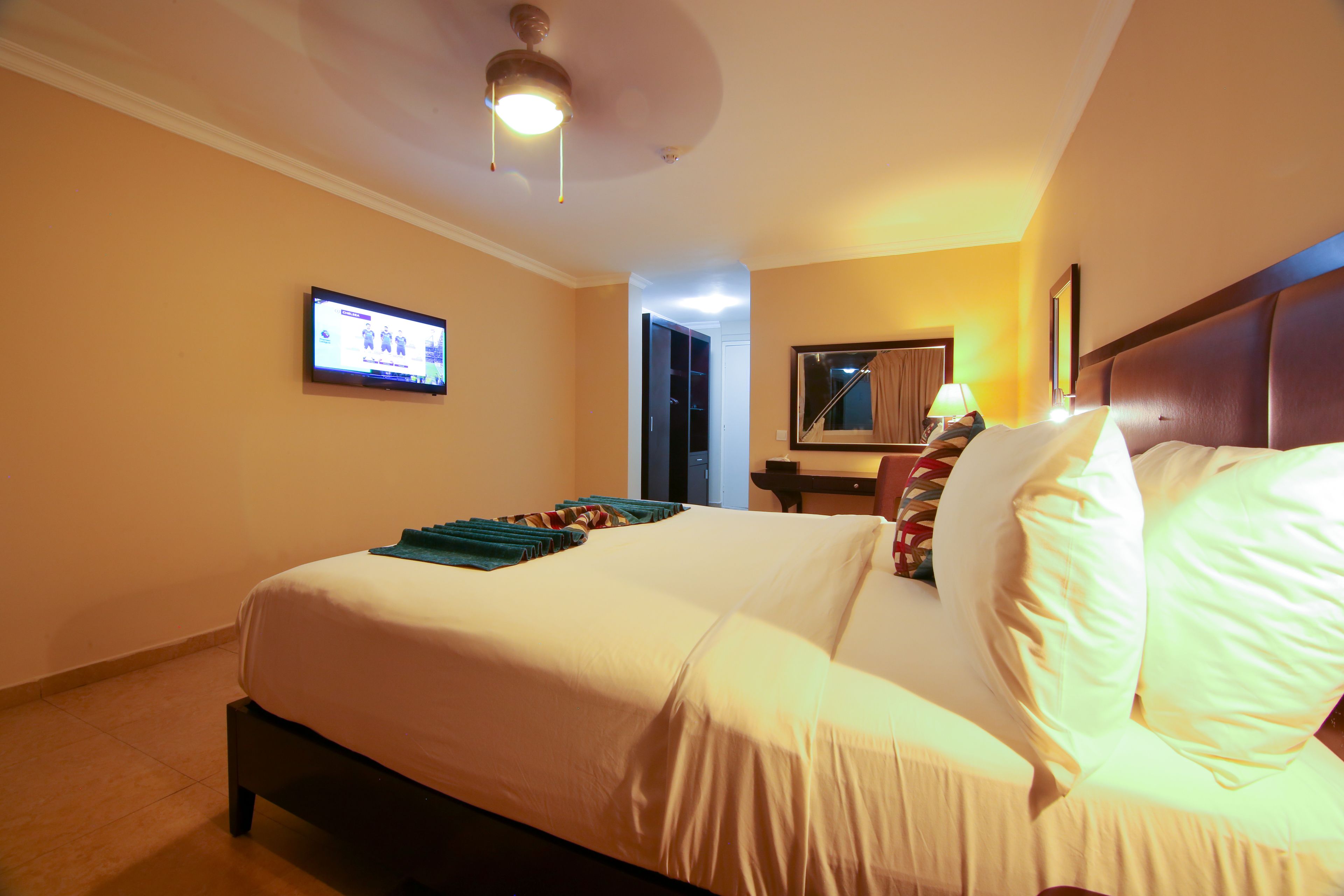 Quarto de hotel com uma cama, uma televisão na parede e um ventilador de teto.