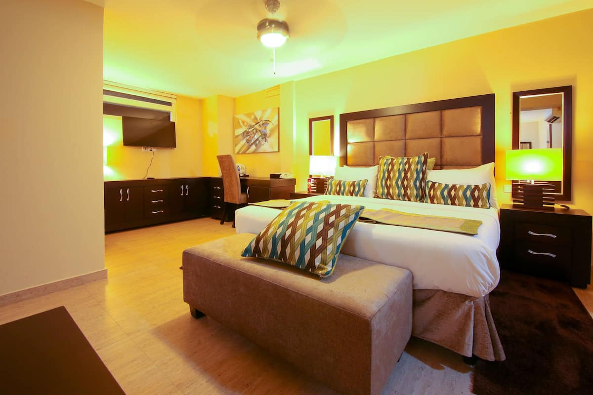 A hotel room with a large bed, a TV mounted on the wall, a desk with a chair, and a sofa.