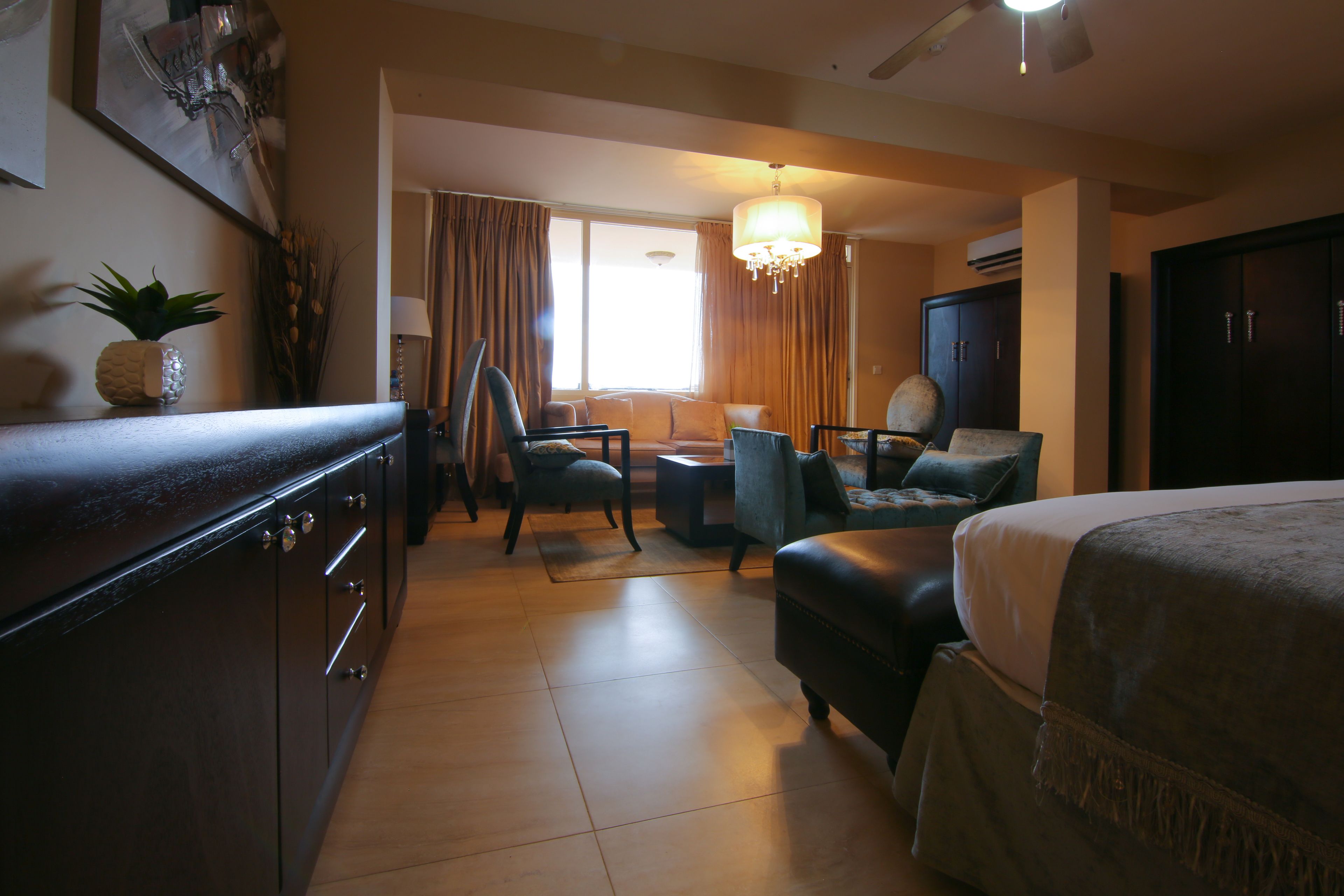 A hotel room with a bed, two armchairs, a small table, a lamp, and a decorative plant.