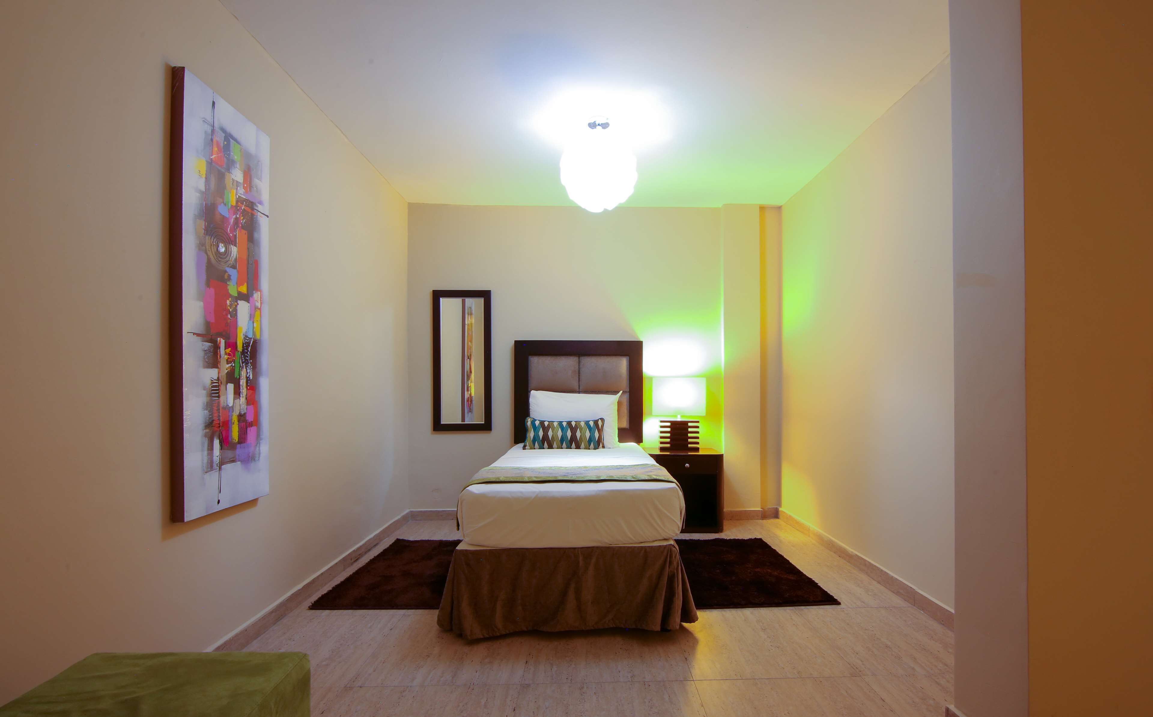 Una habitación de hotel con una cama, una mesita de noche, una lámpara, un cuadro enmarcado y una alfombra.